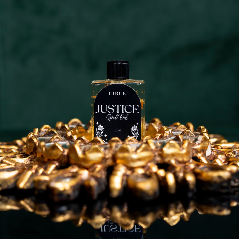 Circe Justice Spell Oil bottle surrounded by gold coins on a dark background
