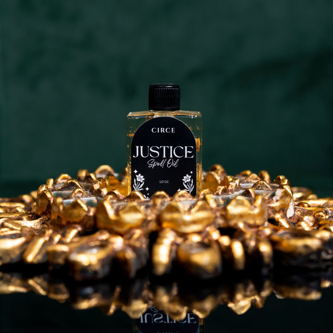 Circe Justice Spell Oil bottle surrounded by gold coins on a dark background