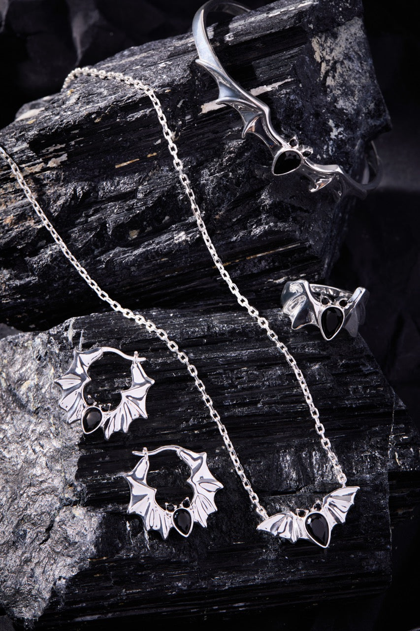 Silver jewelry bat set including necklace, earrings, and ring on dark stone surface