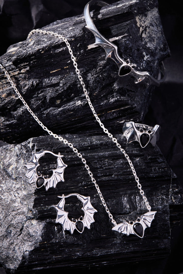 Silver jewelry bat set including necklace, earrings, and ring on dark stone surface