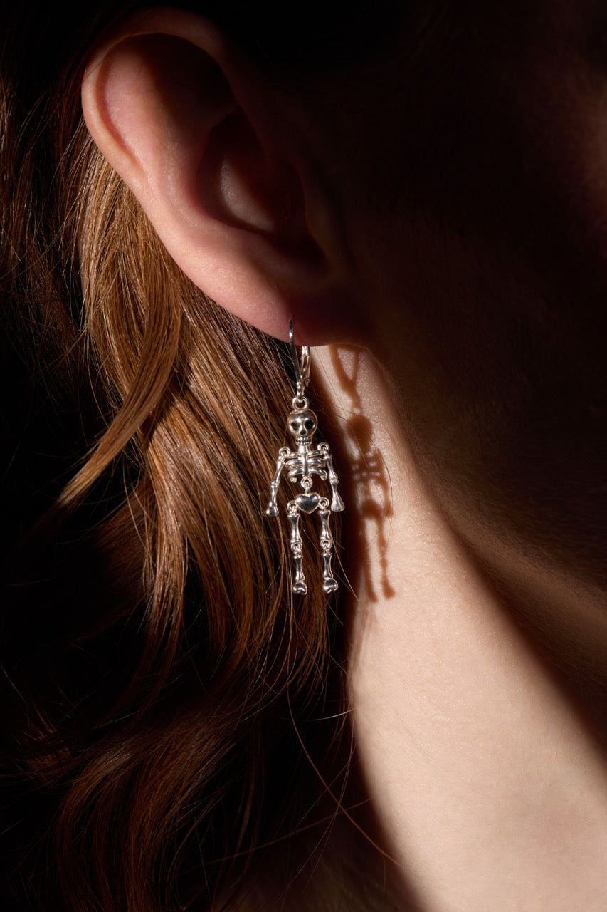 Close-up of a person wearing a skeleton-themed earring with a dark background