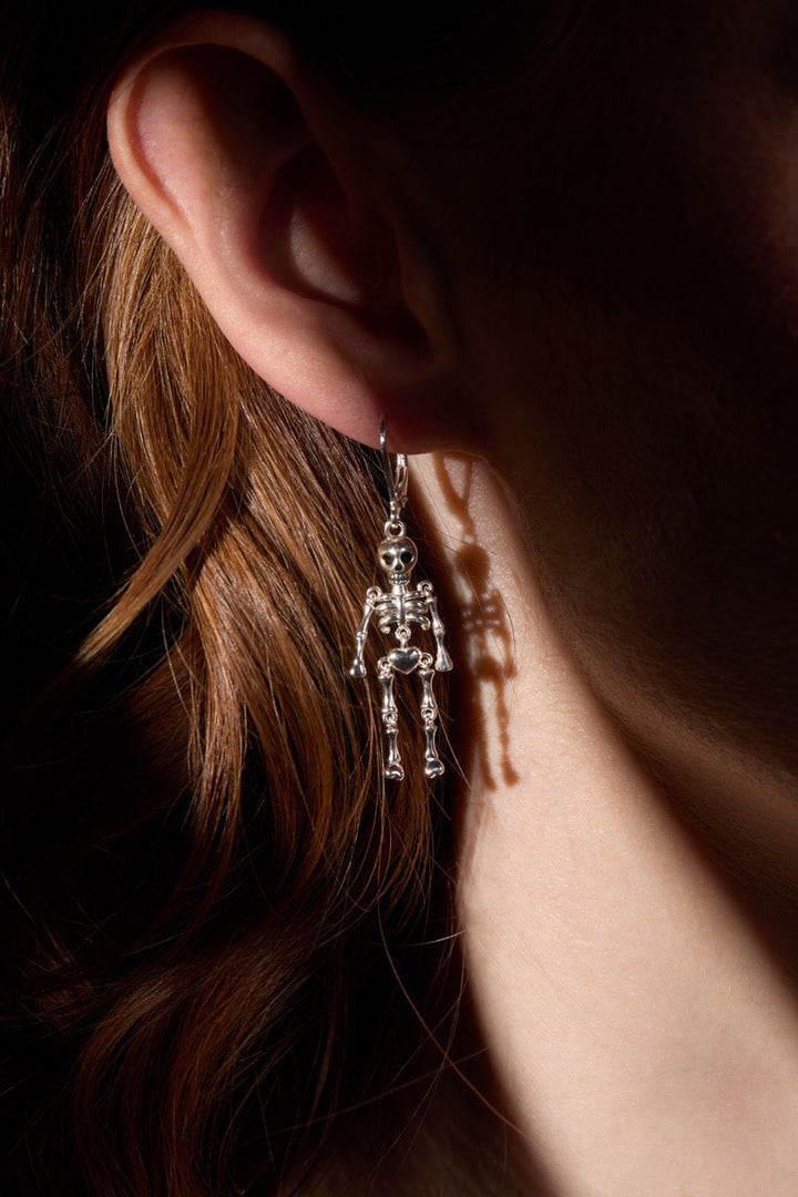 Close-up of a person wearing a skeleton-themed earring with a dark background