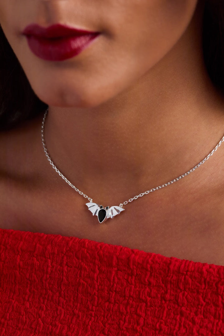Close-up of a woman wearing a silver necklace with a black pendant, against a blurred background.