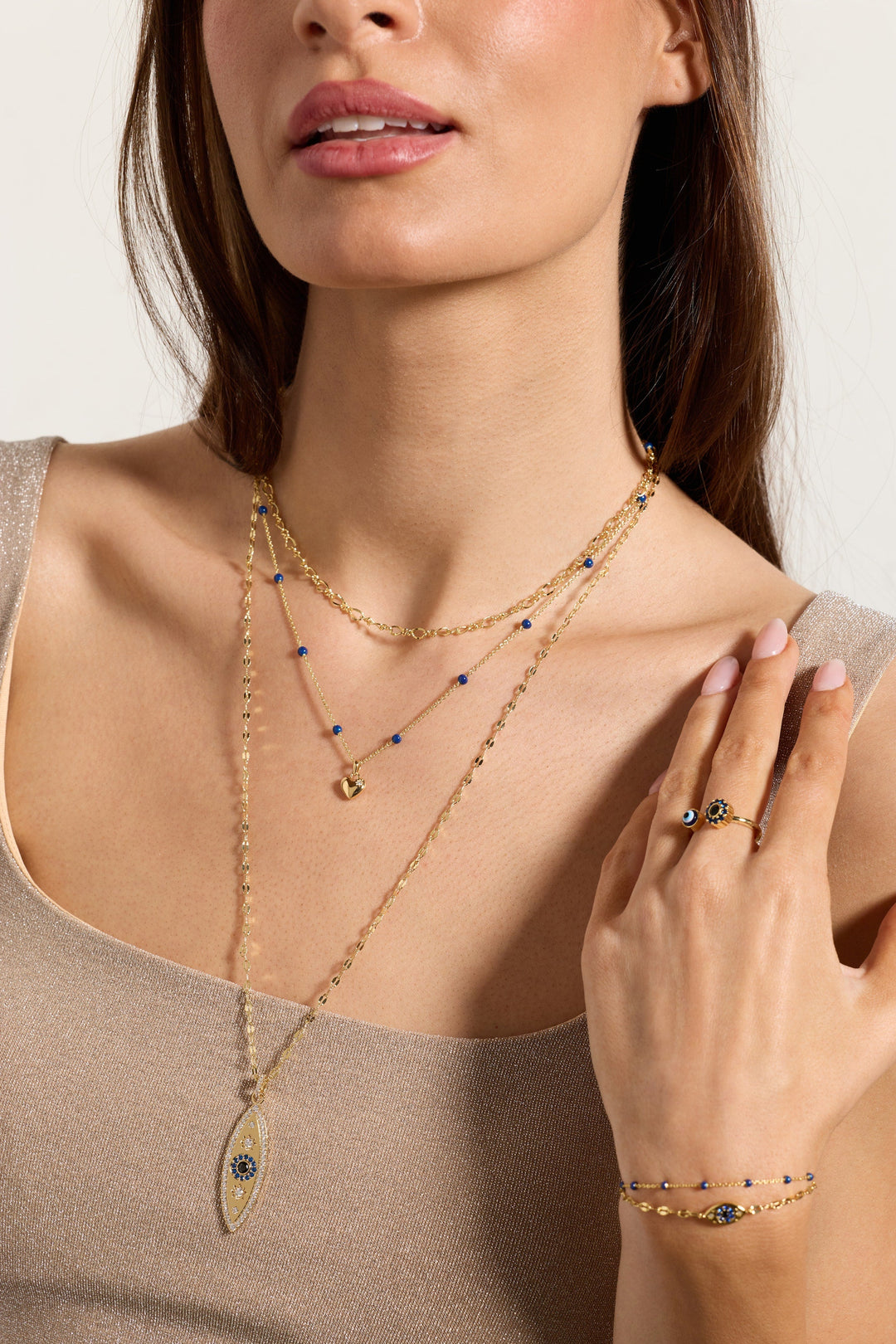 Woman wearing gold necklaces, bracelet, and ring on a neutral background