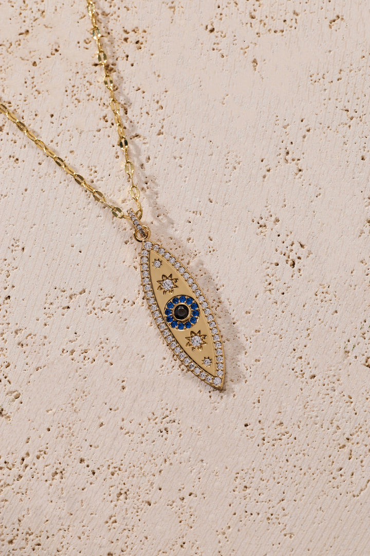 Gold necklace with an eye-shaped pendant on a beige textured background