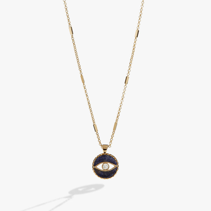 A gold chain necklace featuring a circular pendant with a dark navy blue enamel background and a central gold eye motif with a clear stone, shown against a light gray background.