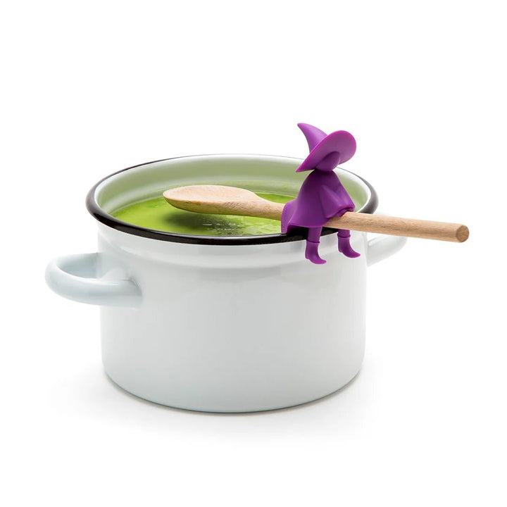 Purple witch spoon rest on a wooden spoon over a pot of green liquid.