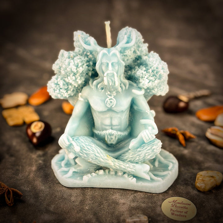Beeswax Horned God Spell Candle with teal wings, raised flame, and hands holding charm.