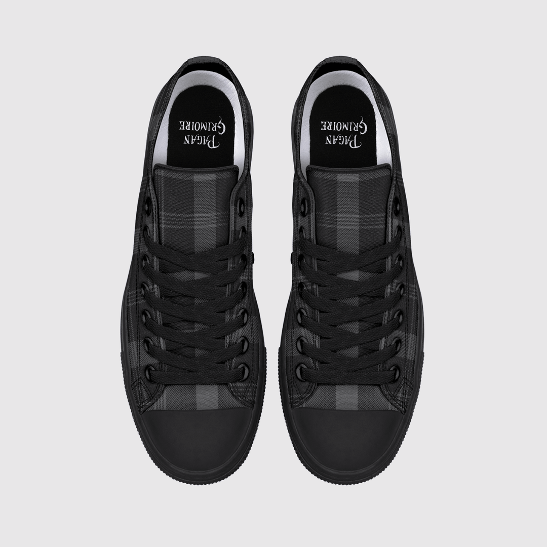 A pair of black low-top sneakers shown from a top-down view on a light gray background. The shoes feature black laces, a black rubber toe cap, and a black and gray plaid pattern on the side panels.
