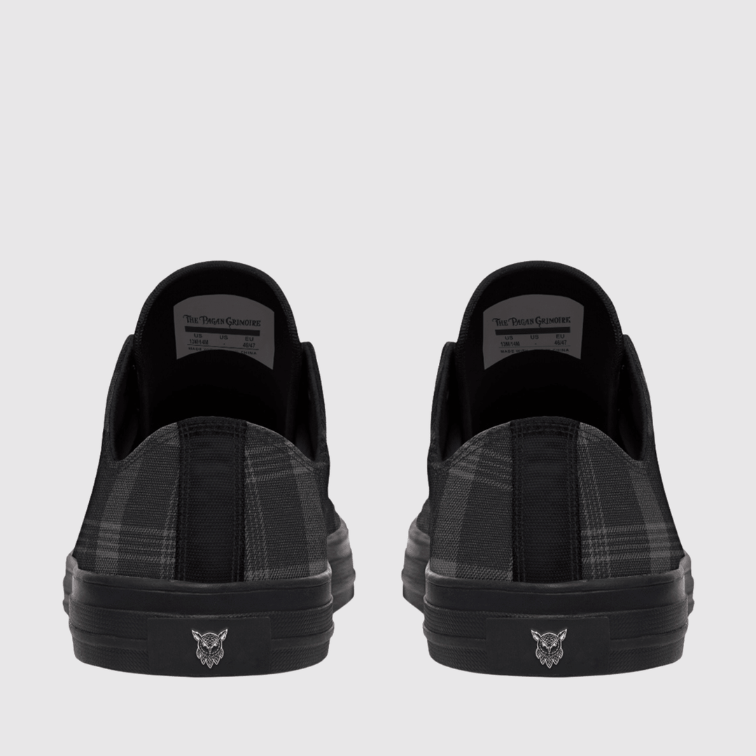 A pair of black slip-on sneakers shown from the back, featuring a black and gray plaid pattern on the sides and a small silver wolf head logo on the black rubber soles.
