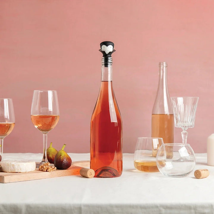 Bottle of rose wine with a cork, two glasses, and a platter with figs and cheese on a pink background