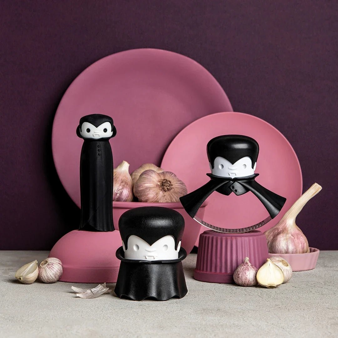 Black and white vampire-shaped garlic press with pink plates and garlic on a purple background
