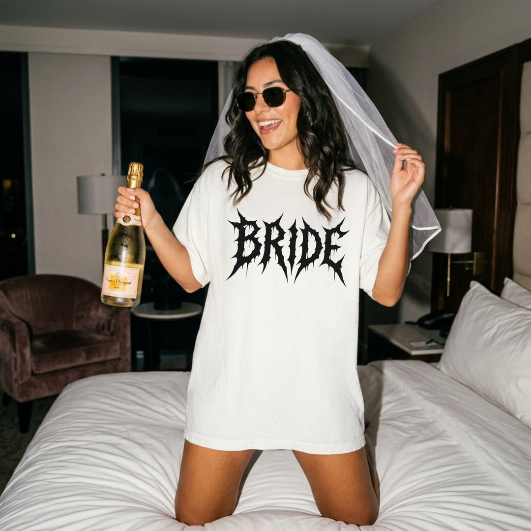Woman in a 'Bride' t-shirt holding a bottle of champagne in a bedroom setting.
