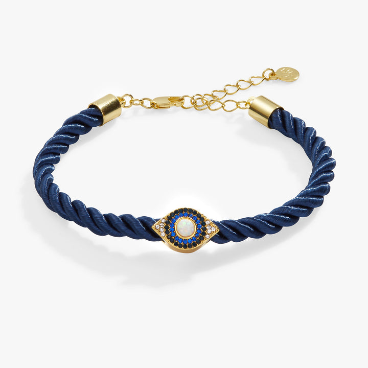 A twisted navy blue cord bracelet with gold-toned hardware, featuring a central gold evil eye charm embellished with blue and white stones, set against a clean white background.