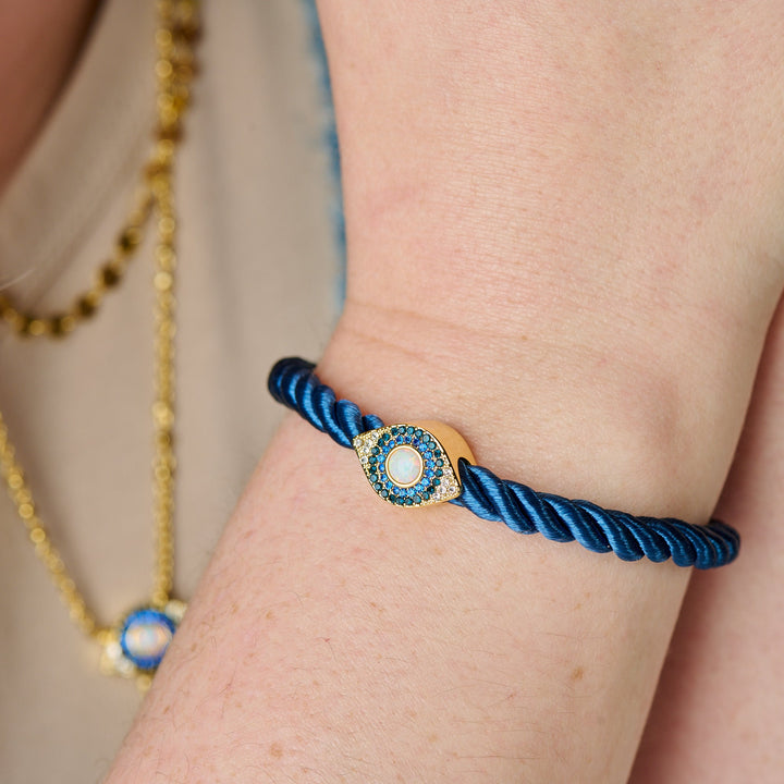 Blue braided bracelet with a gold clasp on a wrist, with a blurred background