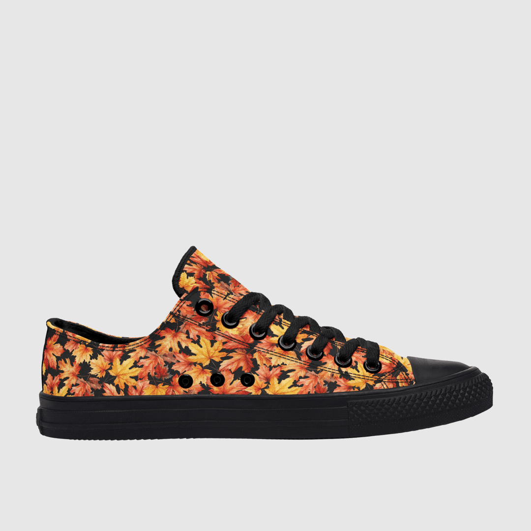 A low-top canvas sneaker featuring a vibrant autumn leaf pattern in orange, yellow, and red, with solid black laces, a black rubber toe cap, and a black sole, shown against a light gray background.