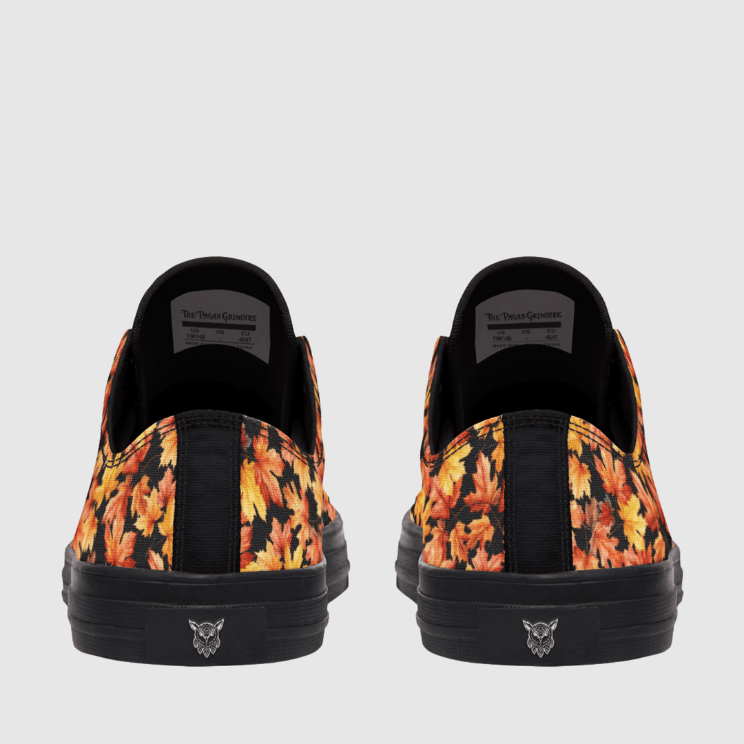 A pair of low-top slip-on sneakers shown from the back, featuring a black base with a vibrant orange, yellow, and red autumn leaf pattern on the sides and a black sole with a small logo.