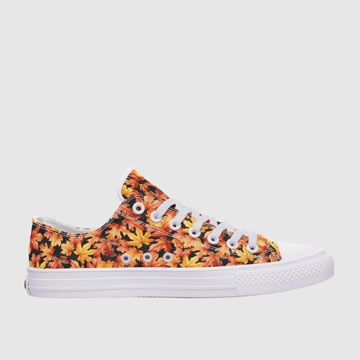 A low-top canvas sneaker featuring an all-over autumn leaf pattern in orange, yellow, and red on a black background, with white laces and a white rubber sole.