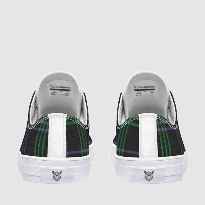 A pair of low-top sneakers shown from the back, featuring a black and green tartan plaid pattern on the sides, a white vertical stripe, and a white rubber sole with a small logo.