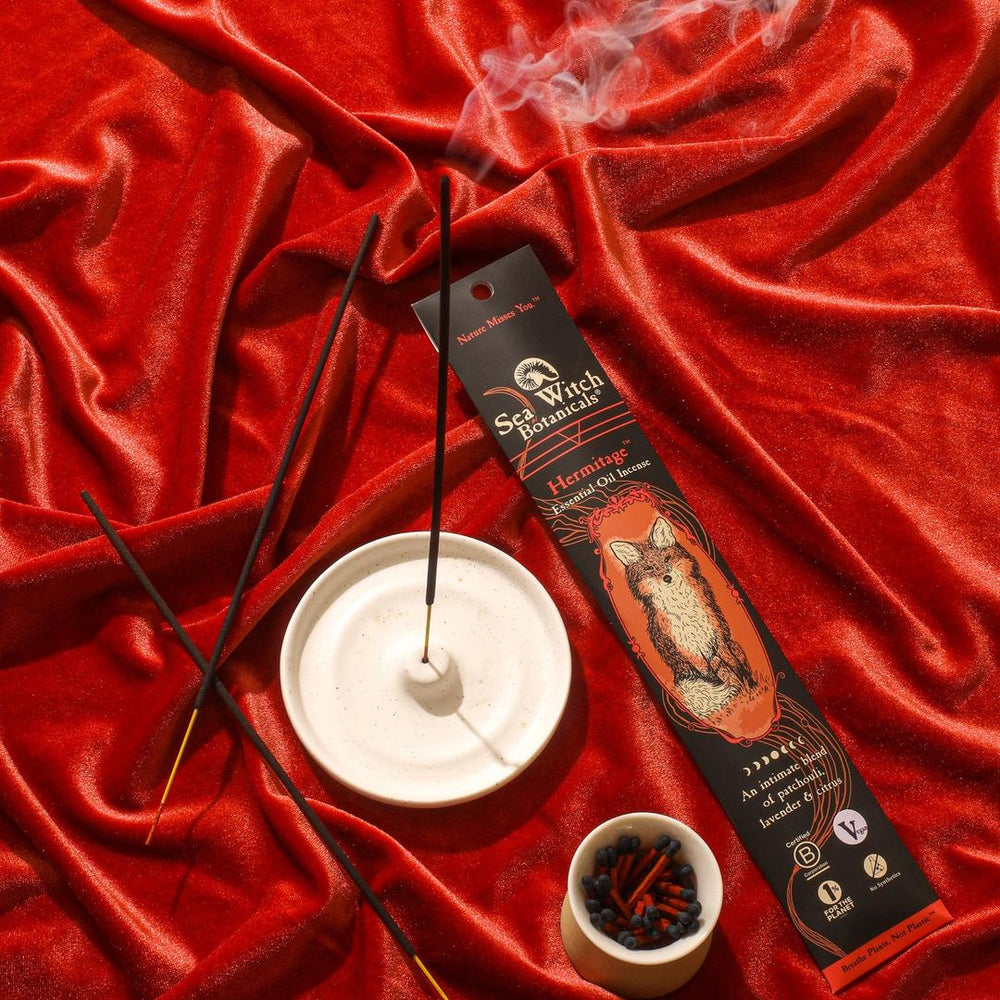 Incense gift set with black sticks, white holder, red satin background.