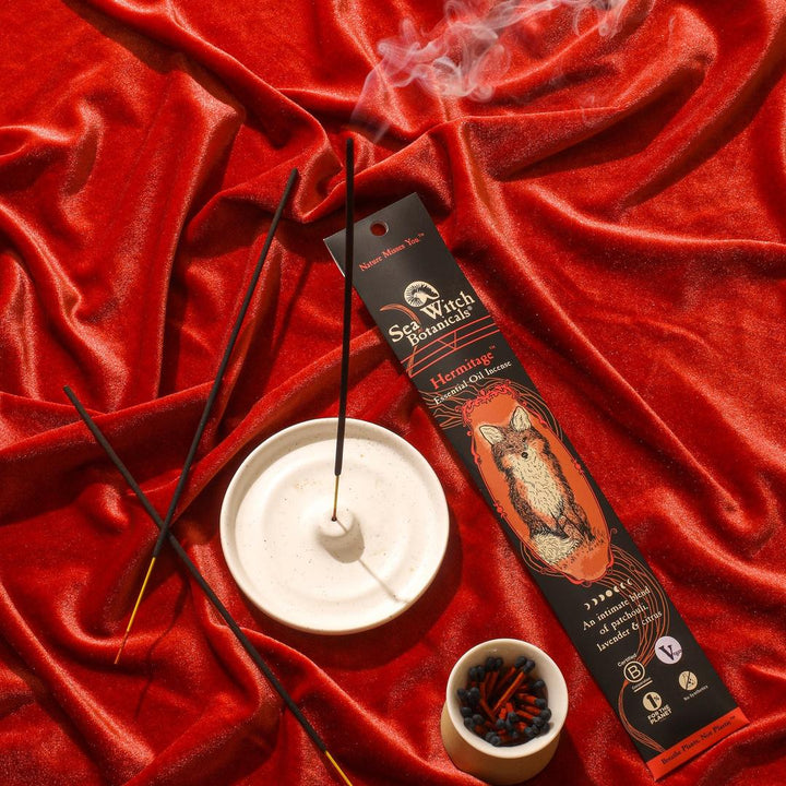Incense gift set with black sticks, white holder, red satin background.