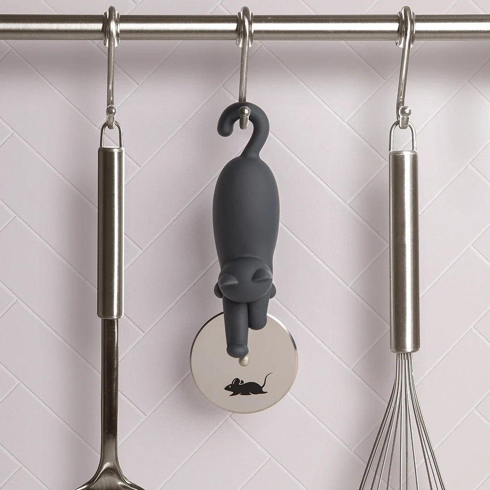 Gray cat-shaped kitchen tool hanging on a rack with a whisk and ladle.