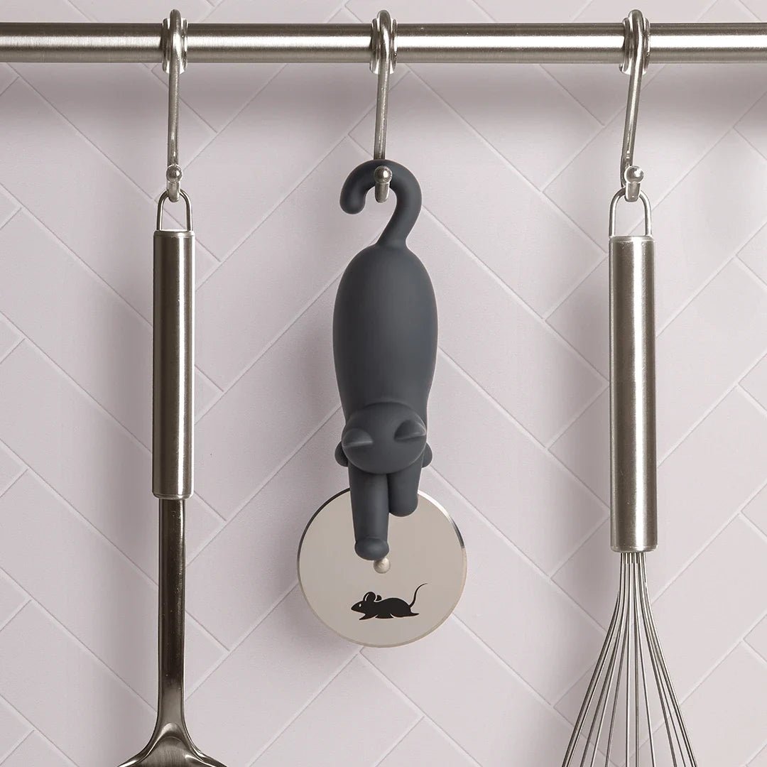 Gray cat-shaped kitchen tool hanging on a rack with a whisk and ladle.