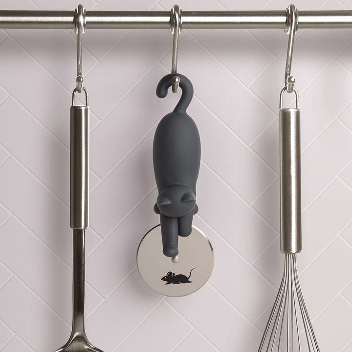 Gray cat-shaped kitchen tool hanging on a rack with a whisk and ladle.
