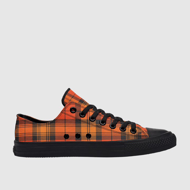 A low-top canvas sneaker featuring a vibrant orange and black tartan plaid pattern on the upper, with a solid black rubber sole, black laces, and black eyelets, shown against a light gray background.