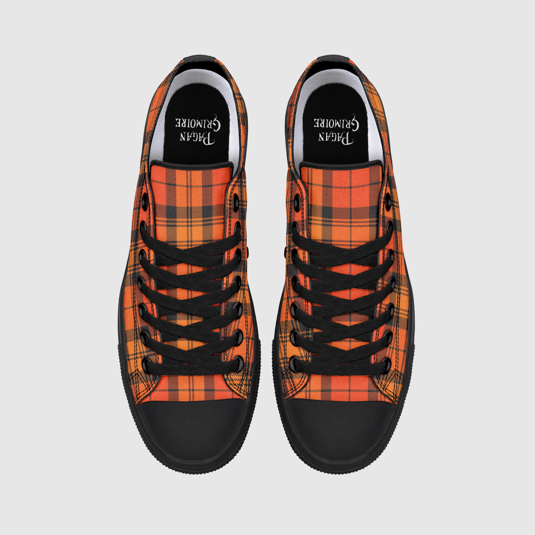 A pair of low-top canvas sneakers shown from a top-down view on a light gray background. The shoes feature a vibrant orange and red tartan plaid pattern, black laces, black rubber toe caps, and a black interior lining with the brand name printed in white.
