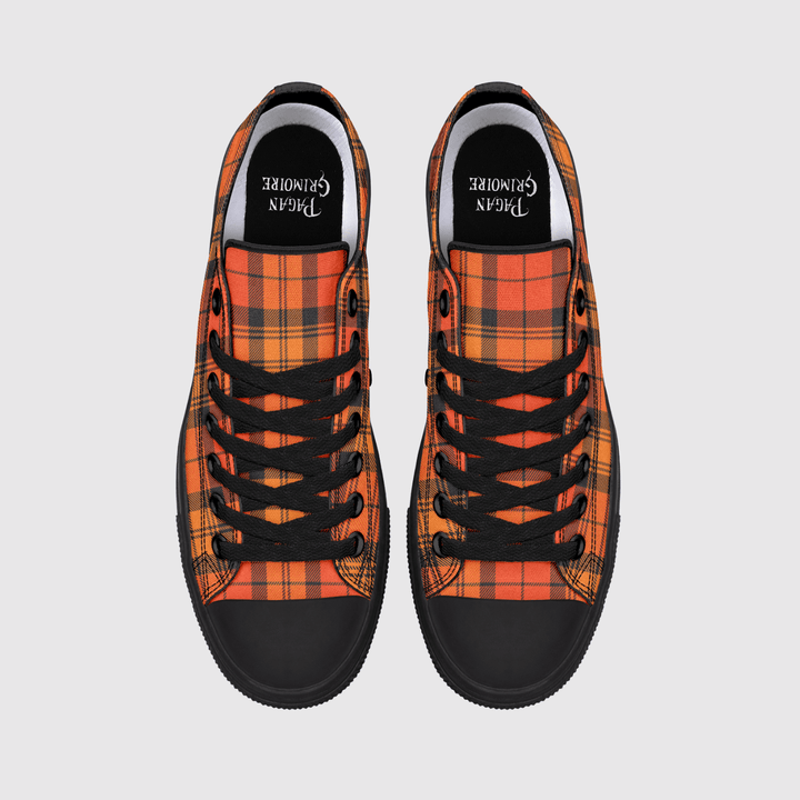 A pair of low-top canvas sneakers shown from a top-down view on a light gray background. The shoes feature a vibrant orange and red tartan plaid pattern, black laces, black rubber toe caps, and a black interior lining with the brand name printed in white.