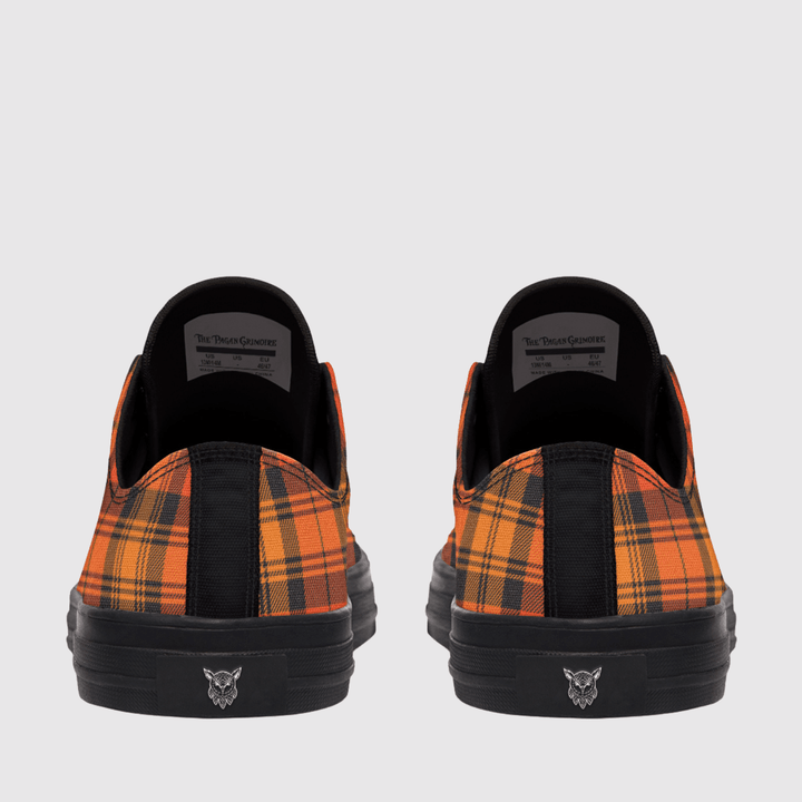 A pair of low-top slip-on sneakers shown from the back, featuring a vibrant orange and black plaid pattern on the canvas uppers, solid black midsoles, and black rubber soles with a small logo.