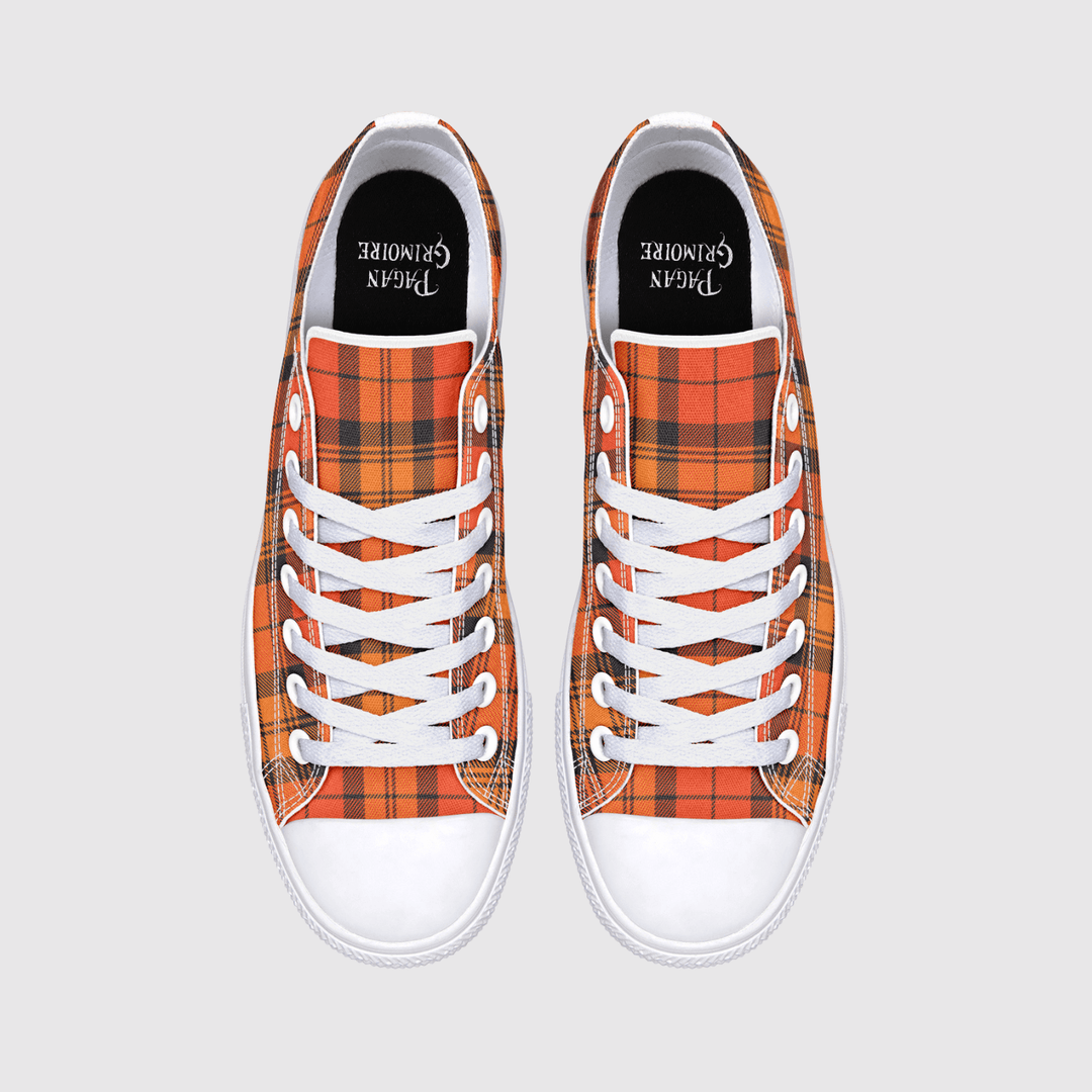 A pair of low-top canvas sneakers shown from a top-down view on a light gray background. The uppers feature a vibrant orange and red tartan plaid pattern with black and yellow lines, white laces, and white rubber toe caps.