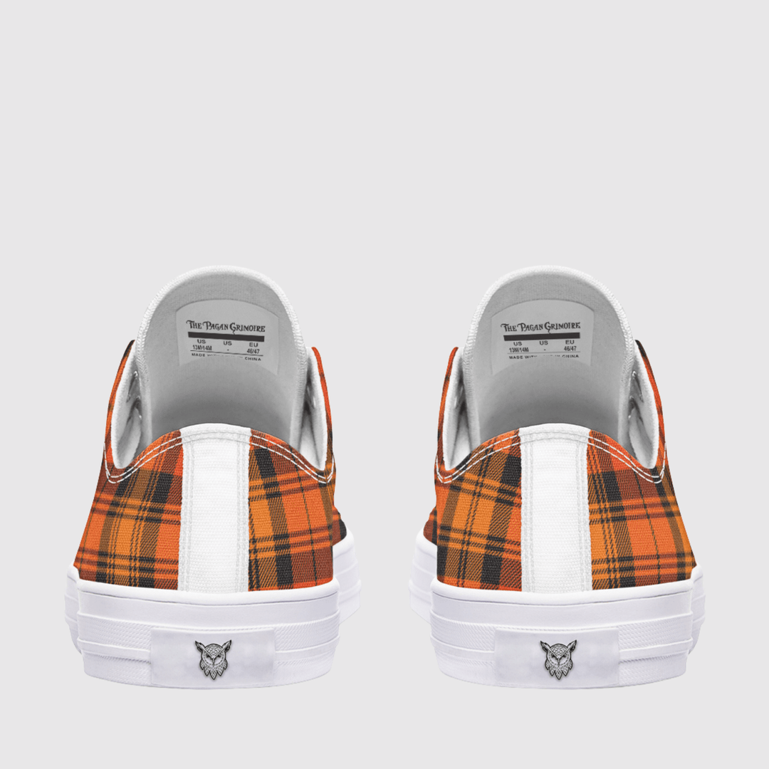 A pair of low-top sneakers shown from the back, featuring orange and black tartan plaid panels, a white vertical stripe, and a white rubber sole with a small logo.