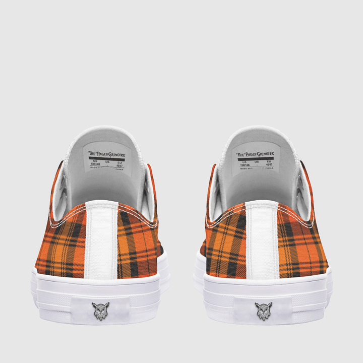 A pair of low-top sneakers shown from the back, featuring orange and black tartan plaid panels, a white vertical stripe, and a white rubber sole with a small logo.