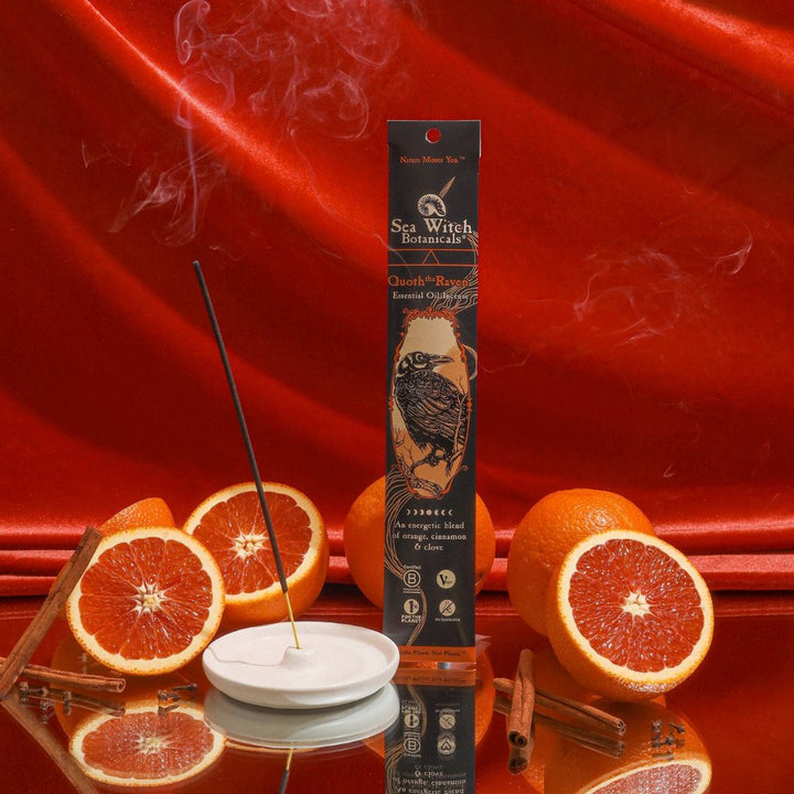 Quoth the Raven incense box stands upright beside burning stick, red citrus slices.
