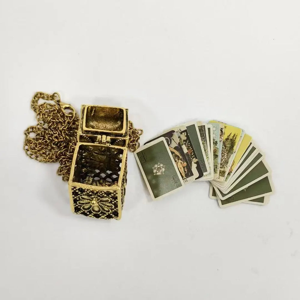 An antique-style gold-toned tarot card chest pendant necklace, shown open with a chain and several tarot cards fanned out beside it on a white background.