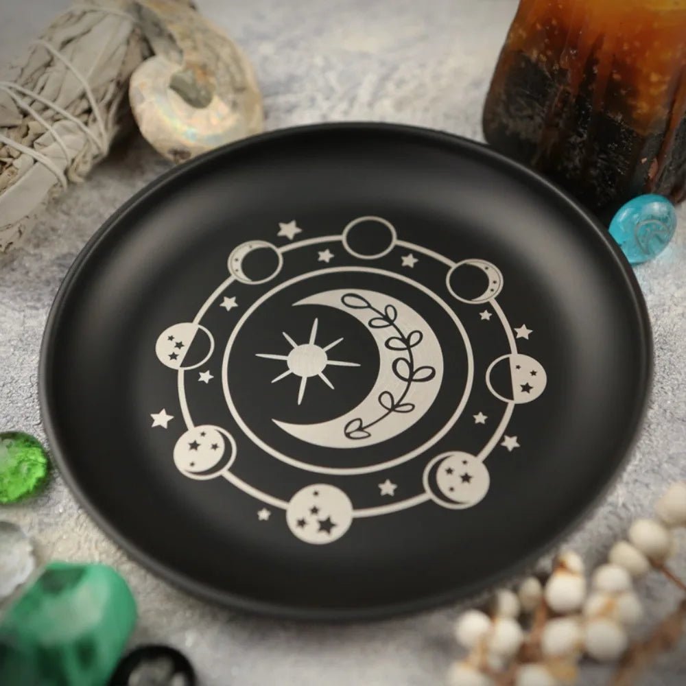 Black plate with white celestial design on a textured surface with decorative items.