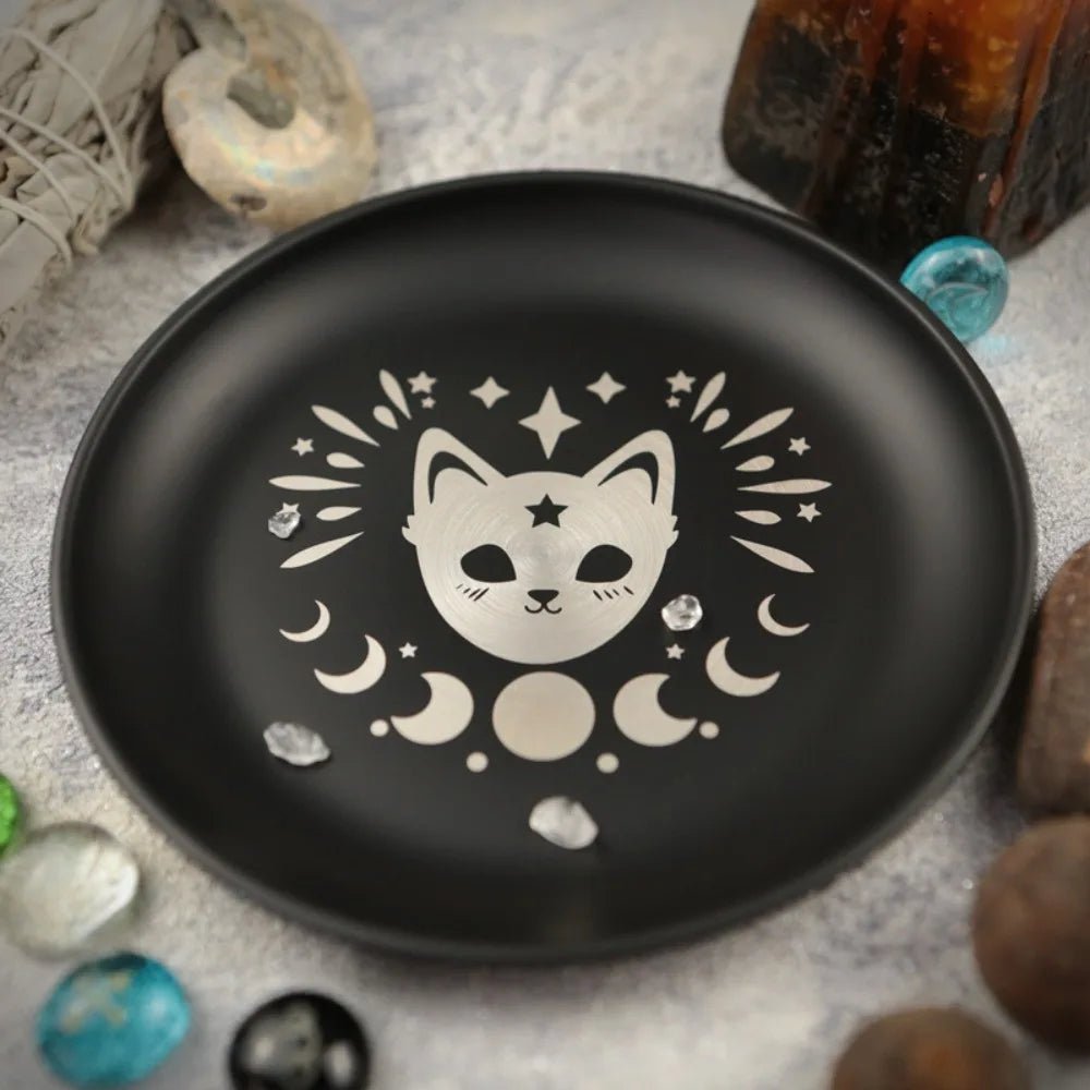 Black plate with a white cat and moon design on a textured surface with stones and crystals.