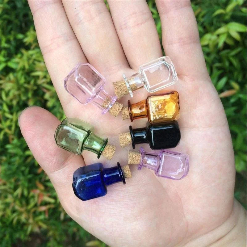 Hand holding small colorful glass bottles with cork lids against a green leafy background