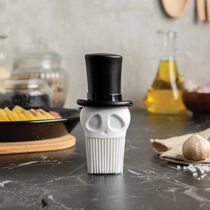 Skull-shaped pepper grinder with a black top hat on a kitchen counter.