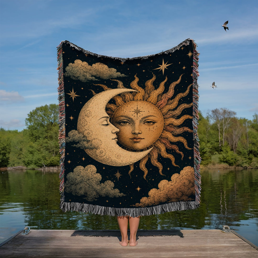 Person holding a tapestry with sun and moon design over a body of water with trees and sky in the background