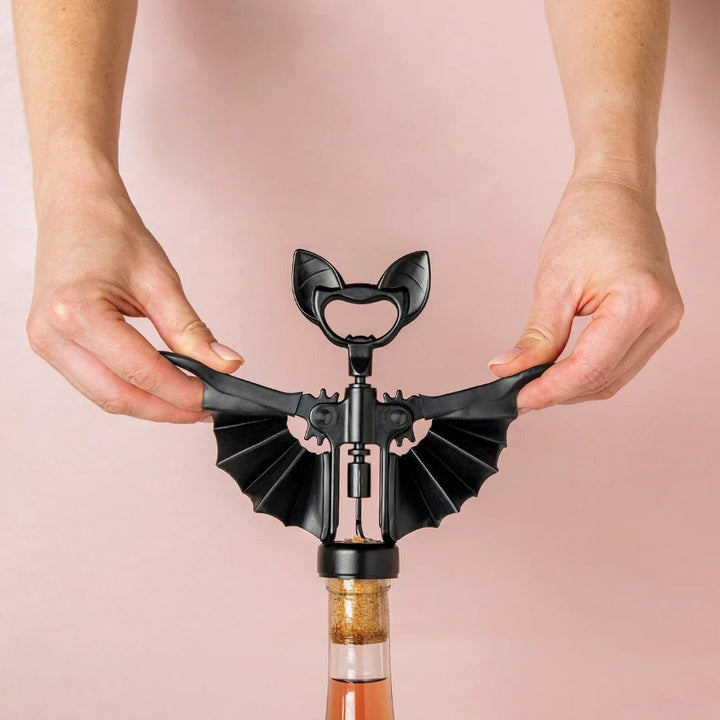 Bat-shaped bottle opener being used on a pink background