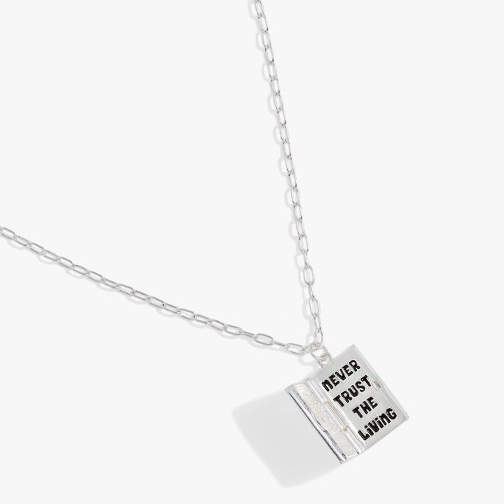 A silver chain necklace with a square pendant engraved with the words 'NEVER TRUST THE LIVING' in black capital letters, shown on a light gray background.