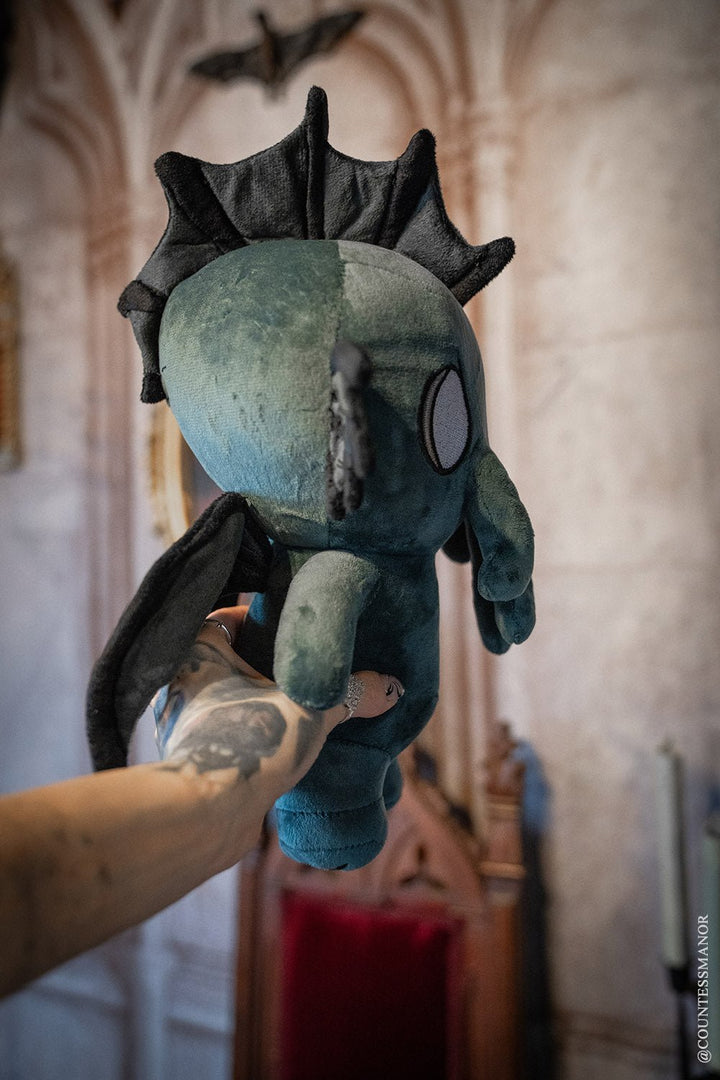 Baby Cthulhu plush in teal with black spiky hood, held upright.