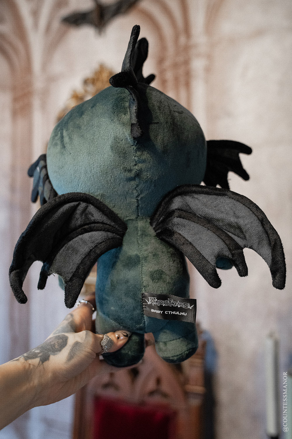 Baby Cthulhu plush in teal fabric with black tentacles, held up.