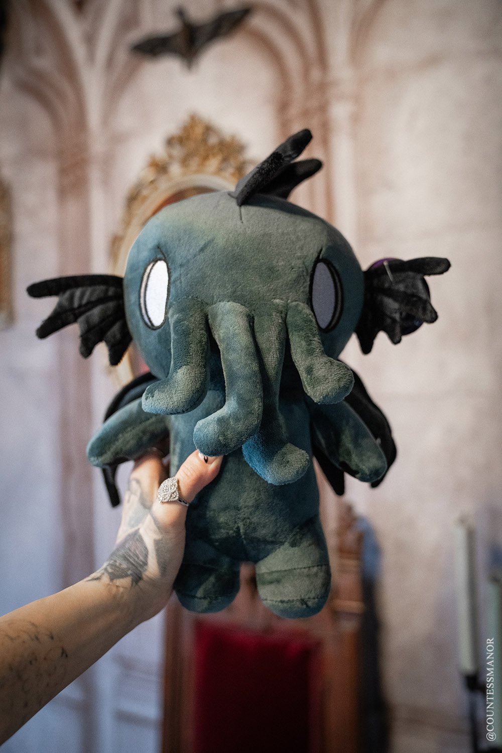 Baby Cthulhu plush toy, teal fabric with black tentacles and big eyes.